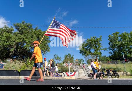 Austin, Texas, USA. Juli 2024. Ein Junge mit einer großen amerikanischen Flagge spaziert auf dem Barton Hills Drive während der jährlichen Parade zum Viertel Barton Hills am 4. Juli in Süd-Austin. Einige hundert Einwohner gingen zu Fuß auf die 1/2 km lange Parade zur Grundschule und genossen Kekse, Wassermelonen und Eis. (Kreditbild: © Bob Daemmrich/ZUMA Press Wire) NUR REDAKTIONELLE VERWENDUNG! Nicht für kommerzielle ZWECKE! Stockfoto