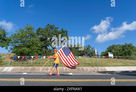 Austin, Tx, USA. Juli 2024. Ein Junge mit einer großen amerikanischen Flagge spaziert am 4. Juli 2024 auf dem Barton Hills Drive während der jährlichen Parade in der Nachbarschaft Barton Hills in Süd-Austin, Texas. Einige hundert Einwohner gingen zu Fuß auf die 1/2 km lange Parade zur Grundschule und genossen Kekse, Wassermelonen und Eis. (Kreditbild: © Bob Daemmrich/ZUMA Press Wire) NUR REDAKTIONELLE VERWENDUNG! Nicht für kommerzielle ZWECKE! Stockfoto