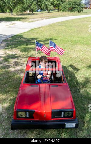 Austin, Tx, USA. Juli 2024. Ein Junge, der in einem Spielzeugauto sitzt und amerikanische Fahnen fliegt, sitzt in der Barton Hills Elementary während der jährlichen Parade zum Viertel Barton Hills am 4. Juli 2024 in Süd-Austin, Texas. Einige hundert Einwohner gingen zu Fuß auf die 1/2 km lange Parade zur Grundschule und genossen Kekse, Wassermelonen und Eis. (Kreditbild: © Bob Daemmrich/ZUMA Press Wire) NUR REDAKTIONELLE VERWENDUNG! Nicht für kommerzielle ZWECKE! Stockfoto