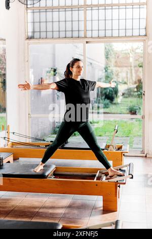 Junge und fitte Frau trainiert Pilates auf Reformerbett. Reformer Pilates Studio-Gerät für Fitnessübungen im Fitnessstudio. Fitnesskonzept. Gesund und s Stockfoto