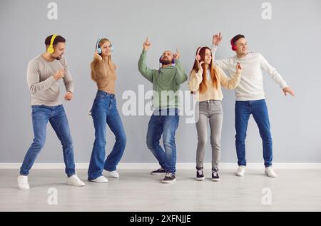 Eine Gruppe unbeschwerter junger Menschen mit modernen Kopfhörern tanzen gerne zu ihrer Lieblingsmusik. Stockfoto