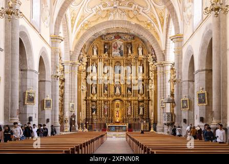 Besucher in der Klosterkirche Santo Domingo de Guzmán, Puebla Mexiko. Verziertes Innenschiff und Altar; historisches Zentrum von Puebla, Puebla Mexiko. Stockfoto