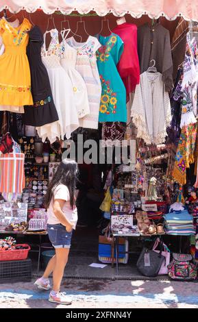 Puebla-Straßenszene; lokale mexikanische Frau, die an einem farbenfrohen Marktstand vorbeiläuft, El Parian Craft Market; Puebla Mexico. Stockfoto