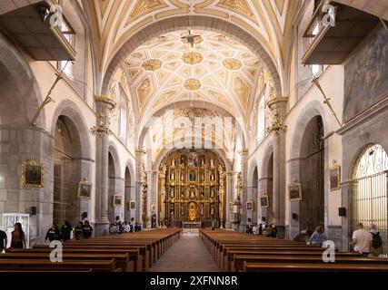 Menschen in der Klosterkirche Santo Domingo de Guzmán, Puebla Mexiko. Verziertes Innenschiff und Altar; historisches Zentrum von Puebla, Puebla Mexiko. Stockfoto