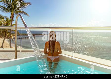 Junge Touristenfrau, die den wunderbaren Horizont des Karibischen Meeres genießt, unter einer strahlenden Sonne, die das kristallklare türkisblaue Wasser reflektiert. Stockfoto