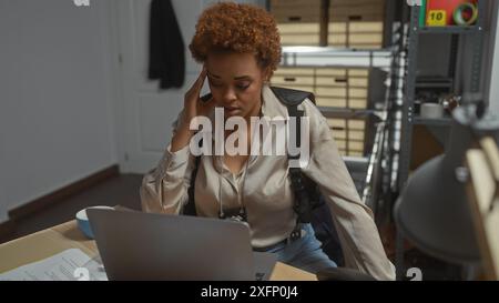 Eine fokussierte afroamerikanische Detektivin, die in einem überfüllten Polizeirevier arbeitet. Stockfoto