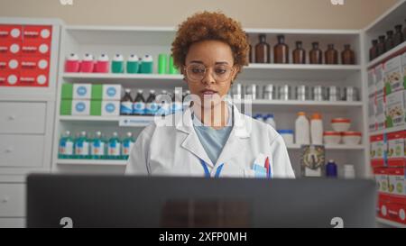 afroamerikanische Apothekerin, die in einer Drogerie arbeitet, umgeben von Regalen mit Medikamenten und Gesundheitsprodukten. Stockfoto