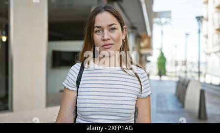 Eine brünette Frau mit blauen Augen und lässiger Kleidung steht nachdenklich auf einer städtischen Straße. Stockfoto
