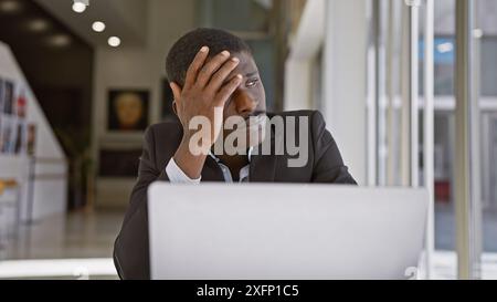 Besorgter afrikanischer Geschäftsmann im Büro, der nachdenkt, während er einen Laptop benutzt. Stockfoto