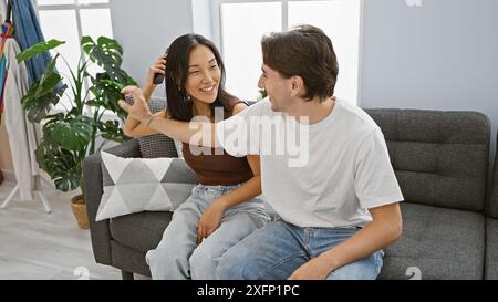 Ein liebevolles, interrassisches Paar genießt einen verspielten Moment zusammen in einem gemütlichen Wohnzimmer. Stockfoto