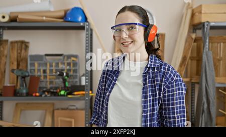 Lächelnde Frau in Sicherheitsausrüstung posiert in einer Tischlerei. Stockfoto