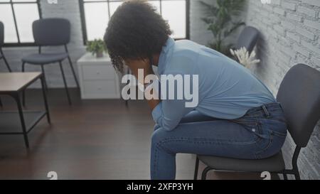 Eine wunderschöne junge afroamerikanische Frau mit lockigen Haaren sitzt besorgt in einem Wartezimmer. Stockfoto