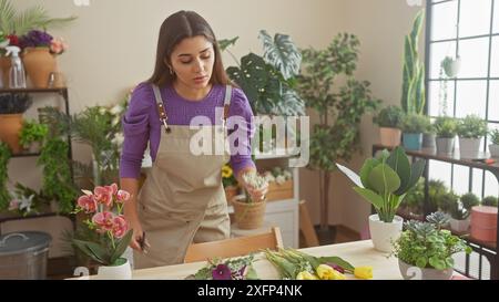 Eine junge hispanische Frau arbeitet aufmerksam in einem Blumenladen, umgeben von verschiedenen grünen Pflanzen und lebendigen Blumen, die Schönheit und Natur im Inneren verkörpern Stockfoto
