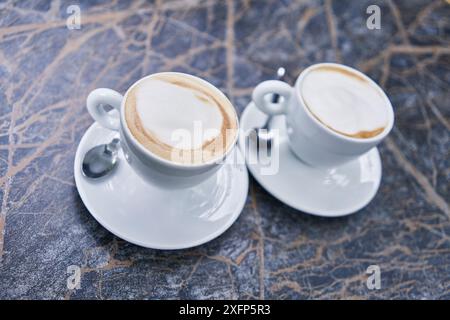 Zwei Cappuccinos mit Milchschaum in weißen Keramikbechern, serviert auf einem Marmortisch und verkörpert ein gemütliches Café-Ambiente. Stockfoto