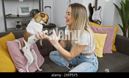 Eine lächelnde junge Frau interagiert spielerisch mit einem Jack russell Terrier in einem gemütlichen Wohnzimmer Stockfoto