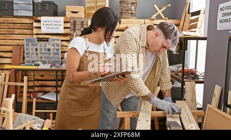 In einer gut ausgestatteten Werkstatt arbeiten eine Frau und ein Mann, beide Zimmerleute, an einem Holzbearbeitungsprojekt zusammen, untersuchen Pläne und bauen einen Stuhl zusammen. Stockfoto