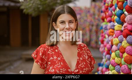 Fröhliche hispanische Frau, strahlend von natürlicher Schönheit, steht selbstbewusst vor yasaka koshindo, lächelnd sorglos in bunter Tradition, ihr Ausdruck Stockfoto