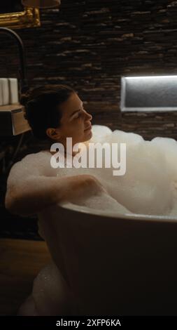 Entspannte Frau, die ein Sprudelbad in einem gut beleuchteten, ruhigen Badezimmer genießt Stockfoto