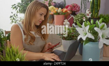 Eine junge blonde Frau benutzt ein Handy in einem Blumenladen, umgeben von verschiedenen Pflanzen und Blumen. Stockfoto