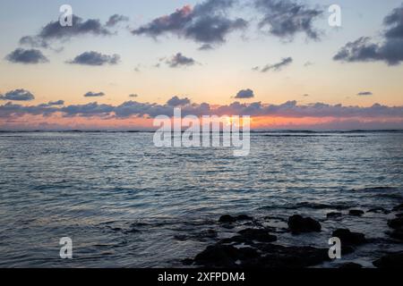 Kleine Wellen umgeben Lavasteine mit Wasser am Meer. Küste einer Insel im Indischen Ozean. Sonnenaufgang am Morgen, wunderschönes warmes Licht an Stockfoto