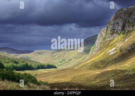 Berglandschaft mit dunklen Regenwolken, die über sonnigen Hanglagen und Tal in Wester Ross, Scottish Highlands, Schottland, Großbritannien, Mai 2017 Stockfoto