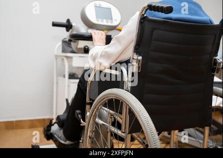 Eine nicht erkennbare ältere Frau macht Pedalübungen vom Rollstuhl aus im Krankenhaus. Hochwertige Fotos Stockfoto