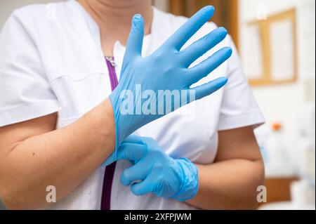 Nahaufnahme einer Krankenschwester, die einen blauen Latexhandschuh auf einen Klinikhintergrund legt. Hochwertiges Foto Stockfoto