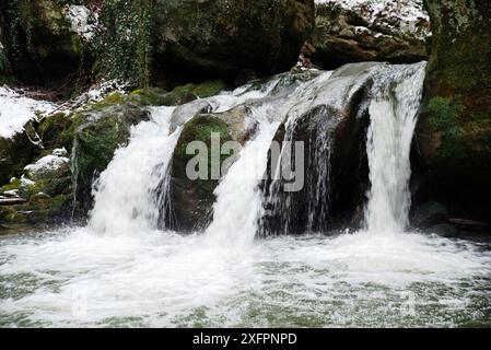 Wasserfall, Schwarzer Ernz mit schneebedeckter Steinbrücke, Müllerthal-Wanderweg in Waldbillig, Luxemburg im Winter Stockfoto