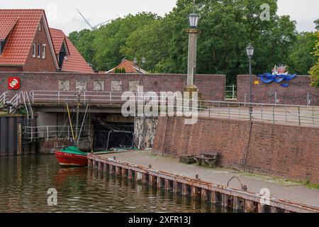 Ein kleines Hafengebiet mit einem rot-grünen Boot vor einer Backsteinmauer und grünen Bäumen im Hintergrund, wangerland, niedersachsen, deutschland Stockfoto