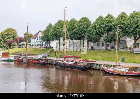 Die Boote legten friedlich an den Ufern eines ruhigen Kanals an. Die Ufer sind gesäumt von grünen Bäumen und charmanten Häusern, carolinensiel, niedersachsen, deutschland Stockfoto