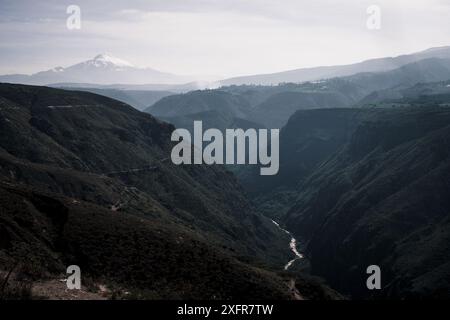 Dramatischer Blick auf die Andenschlucht in Ecuador, mit einem sich windenden Fluss und einem schneebedeckten Vulkan im Hintergrund, der die raue Schönheit und den Teppich einfängt Stockfoto