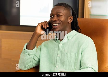 Lächelnder Mann, der auf dem Smartphone spricht, während er im Bürostuhl sitzt Stockfoto