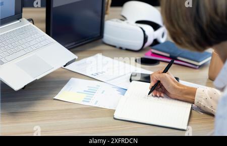 Schreiben in Notizblock, Frau, die am Schreibtisch mit Laptop und Dokumenten arbeitet Stockfoto