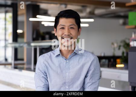 Ein lächelnder Mann im Büro trägt ein blaues Hemd und blickt selbstbewusst in die Kamera Stockfoto