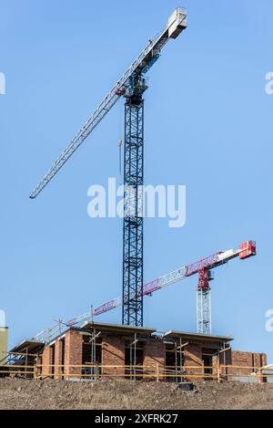 Ein Paar Bauturmkrane, die auf der Baustelle auf blauem Himmel arbeiten Stockfoto