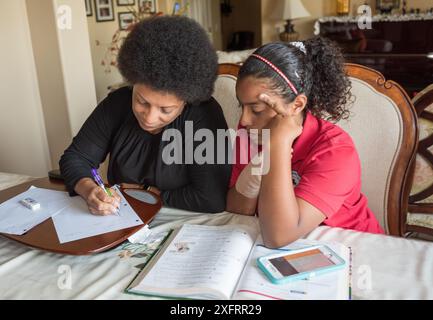 Afroamerikanische Mutter hilft Tochter bei Hausaufgaben am Esstisch. Stockfoto