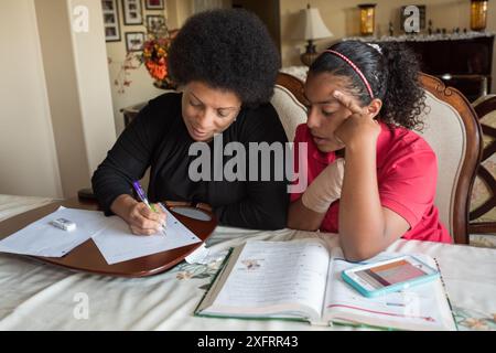 Afroamerikanische Mutter hilft Tochter bei Hausaufgaben am Esstisch. Stockfoto