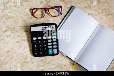 Das Wort SPENDE steht auf einem Taschenrechnerdisplay und einem hellen Hintergrund mit einem Notizblock zum Schreiben Stockfoto