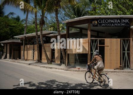 Tulum, Mexiko. Juli 2024. Eine Frau fährt mit dem Fahrrad vor einem Laden, der von Holzbrettern vor den Auswirkungen des Hurrikans Beryl geschützt ist. Der atlantische Hurrikan wird voraussichtlich am Freitagabend Hurrikan 1 an der Ostküste der Halbinsel Yucatán erreichen. Experten erwarten starke Winde und Regenfälle sowie gefährliche Sturmfluten. Quelle: Felix Marquez/dpa/Alamy Live News Stockfoto