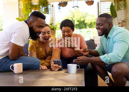 Treffen sich um das Smartphone, verschiedene Freunde lachen und genießen die gemeinsame Zeit zu Hause Stockfoto