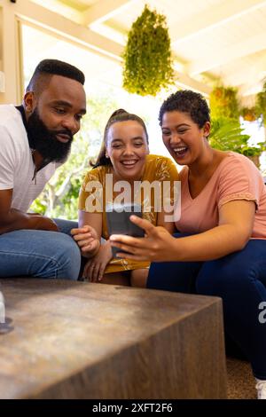 Zusammen sitzen, verschiedene Freunde lächeln und auf den Smartphone-Bildschirm schauen Stockfoto