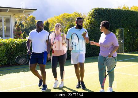 Tennis spielen, eine Gruppe verschiedener Freunde mit Schlägern und Tennisbälle halten, im Freien genießen Stockfoto