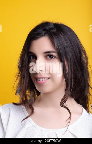 Eine junge Frau mit langen braunen Haaren posiert glücklich auf gelbem Hintergrund und strahlt Freude und Positivität aus Stockfoto