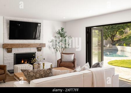 Modernes Wohnzimmer mit Kamin, Fernseher und offener Schiebetür, die zu einem Pool im Hinterhof führt. Stockfoto