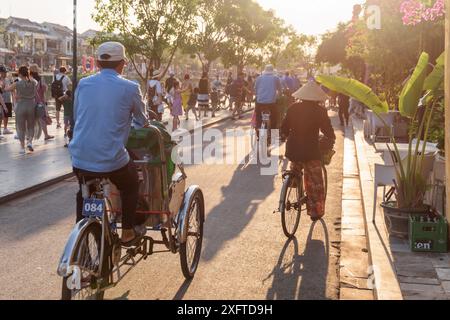 Hoi an (Hoian), Vietnam - 11. April 2018: Fahrradrikschas (Trischas) und Vietnamesin in traditionellem Bambushut auf dem Fahrrad. Stockfoto