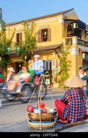 Hoi an (Hoian), Vietnam - 11. April 2018: Vietnamesischer Straßenkostverkäufer in der antiken Stadt. Frau mit traditionellem Bambushut. Stockfoto