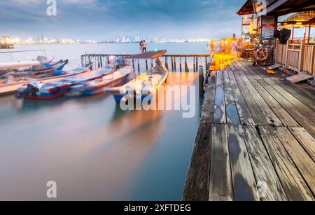 Penang Island, Malaysia - 25. April 2023: Entlang der alten Steg-Promenade, nahe Sonnenuntergang, Besucher stehen, sitzen und fotografieren am Wasser, mit kleinem Motor Stockfoto