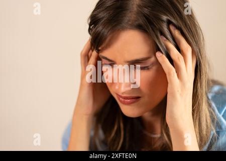 Junge Frau, die Stress und Kopfschmerzen hat und den Kopf vor Schmerzen hält. Emotionale Belastung und Unwohlsein - Stress, Angst, Migräne, emotionale Schmerzen, Stockfoto