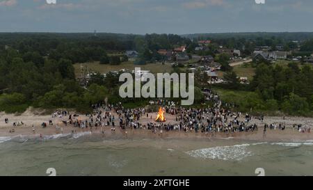 Feier der Mittsommerferien (Ligo) in Pavilosta, Lettland. Viele unerkannte Leute stehen an einem brennenden Feuer in einer Sommernacht im Stockfoto