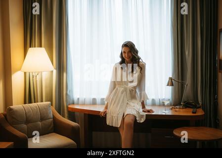 Die Braut macht sich morgens in ihrem Zimmer in einem Bademantel am Fenster fertig Stockfoto